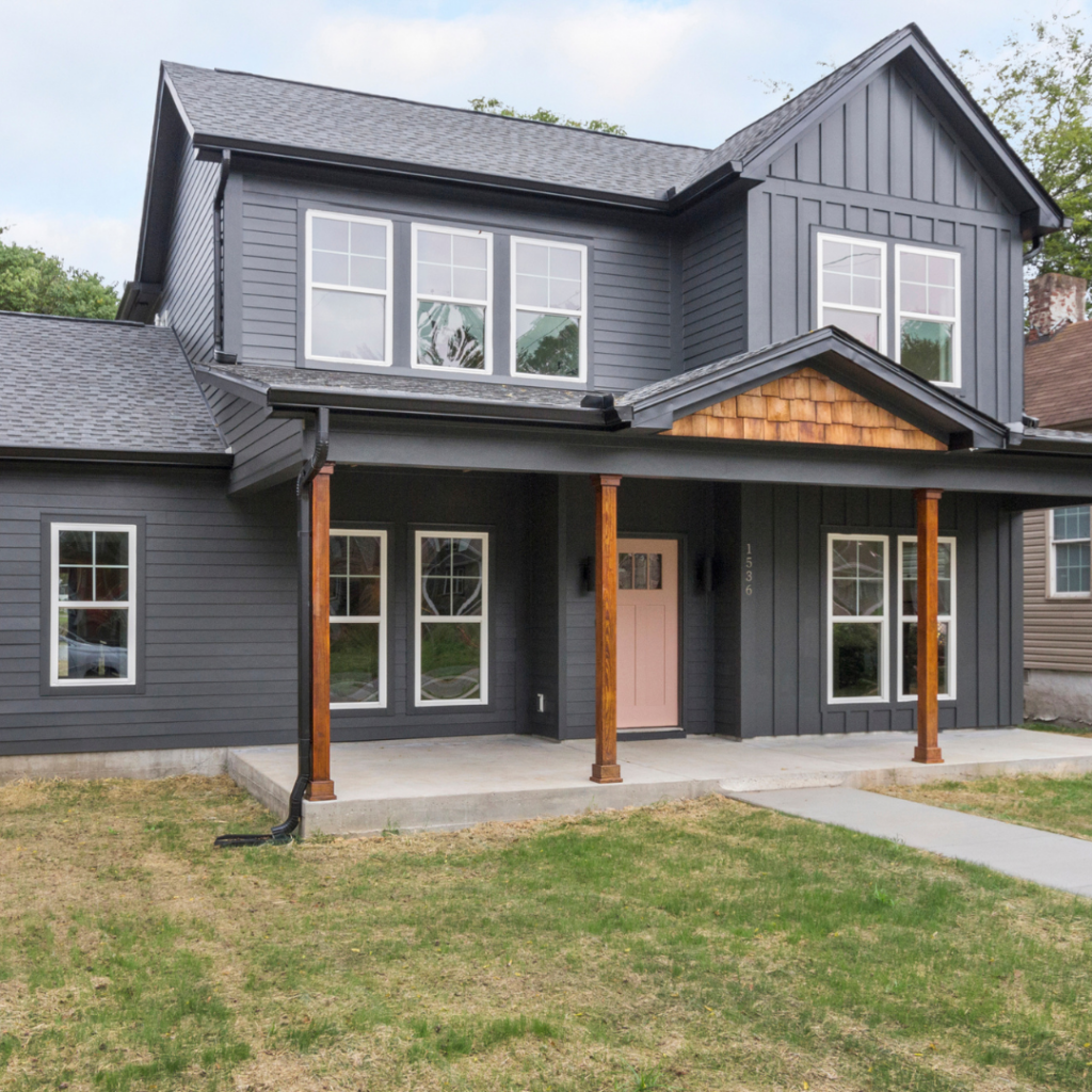 Modern farmhouse-style custom home with dark siding, wood accents, and a pink front door.