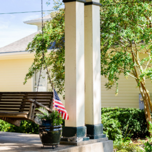 Restored front porch with wooden swing, historic columns, and greenery.